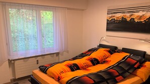 A bedroom with a bed, a window with curtains, a radiator, and a painting on the wall.