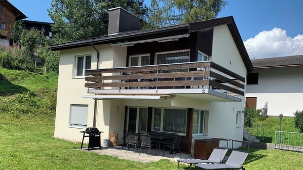 A two-story house with a balcony, outdoor seating, and a barbecue area.