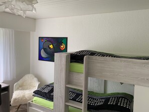 A bunk bed with a green and black mattress, a white furry chair, and a painting on the wall.