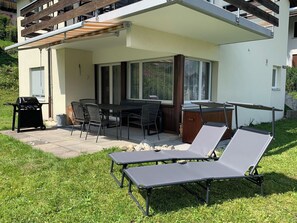 A patio area with a table and chairs, a grill, and two lounge chairs.
