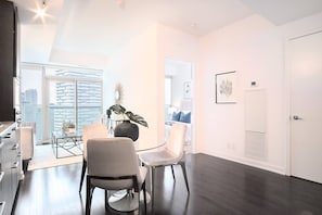 Una sala de estar moderna con una mesa de comedor de vidrio, dos sillas y un amplio ventanal con vista a la ciudad.