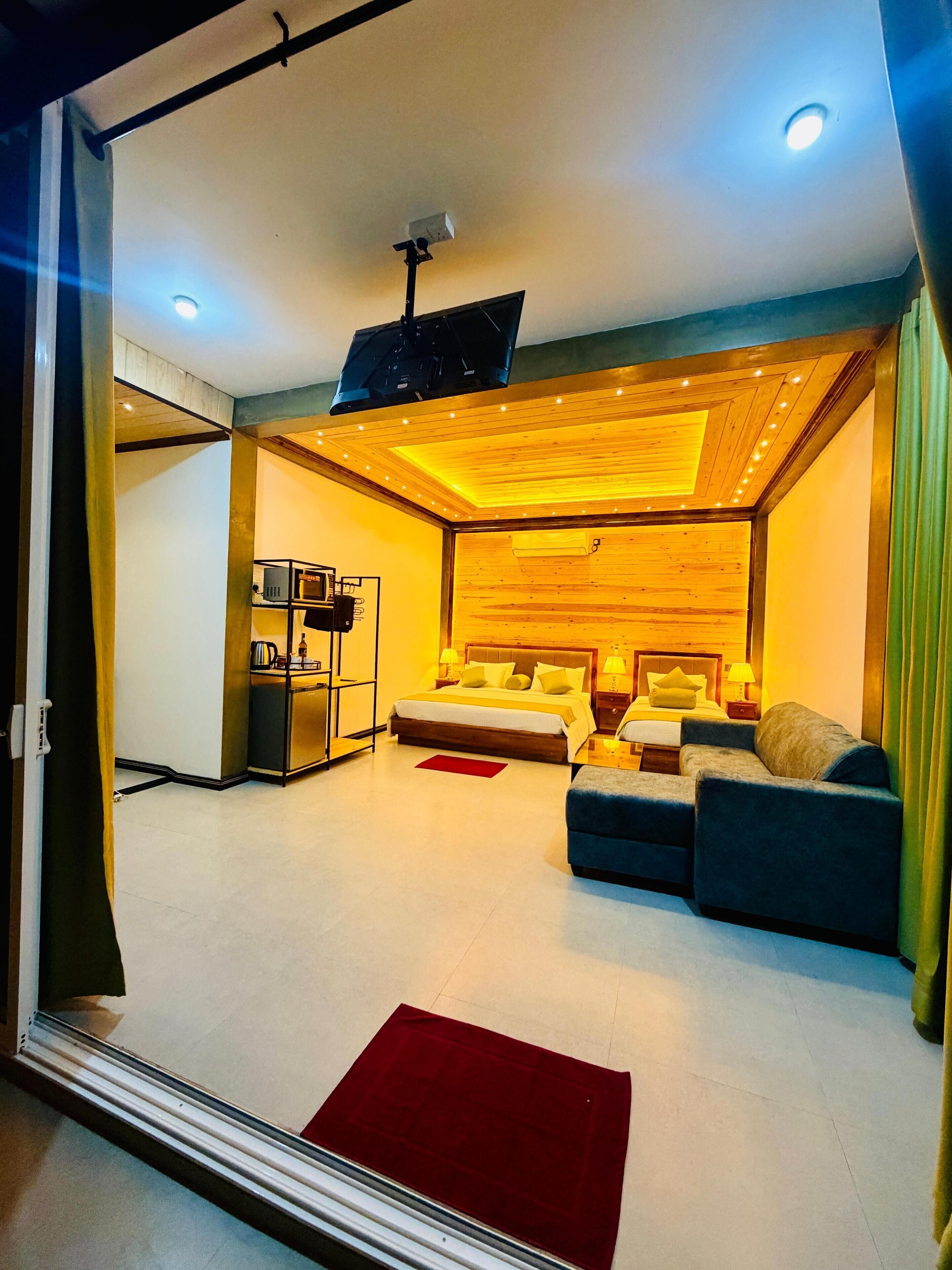 A modern hotel room with a bed, sofa, and a TV mounted on the wall.