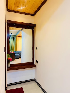 Un pasillo con techo de madera y un espejo grande que refleja una habitación con un sofá azul y una cortina verde.