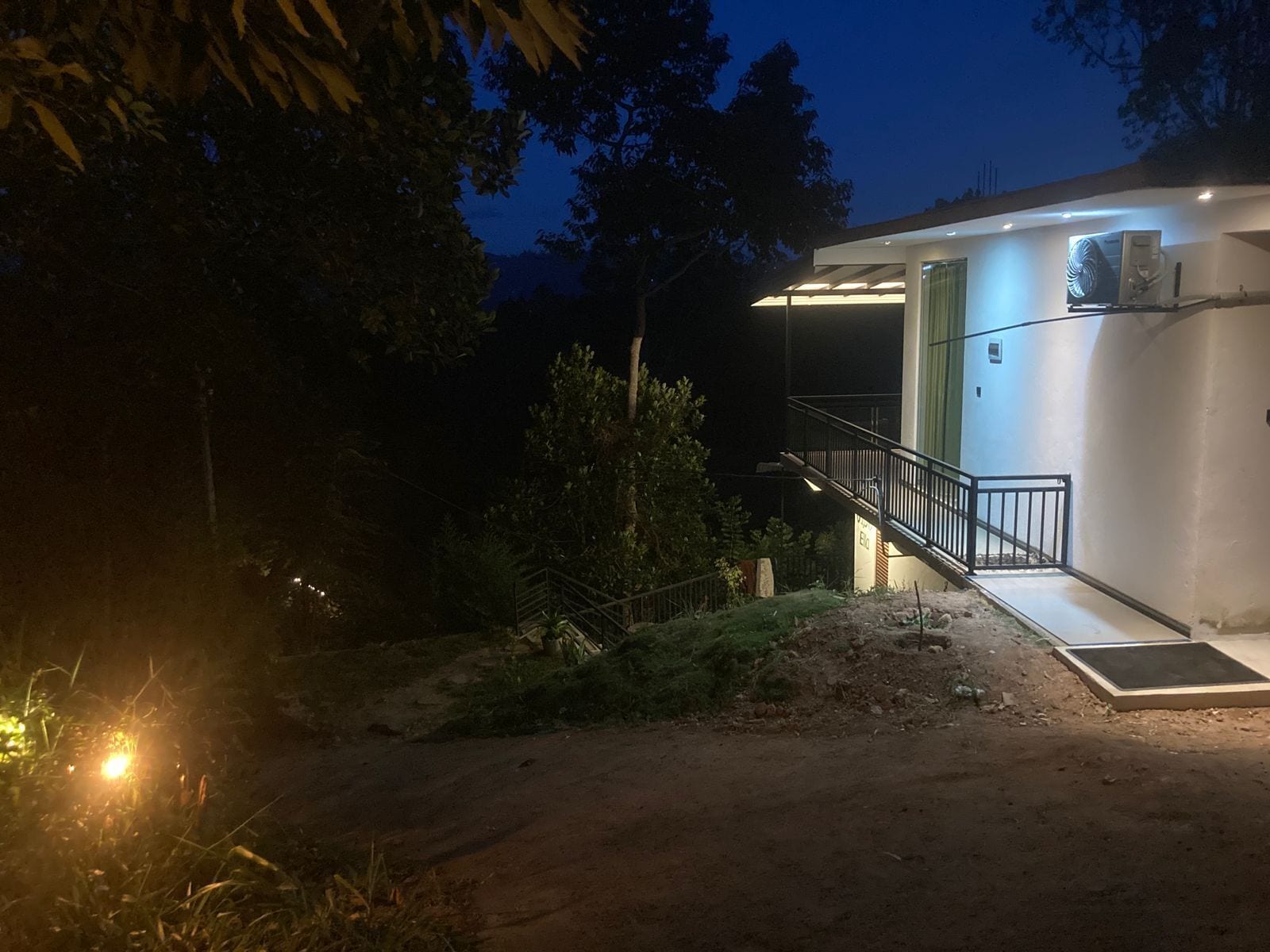 A modern building with a staircase leading to a covered entrance, surrounded by vegetation.