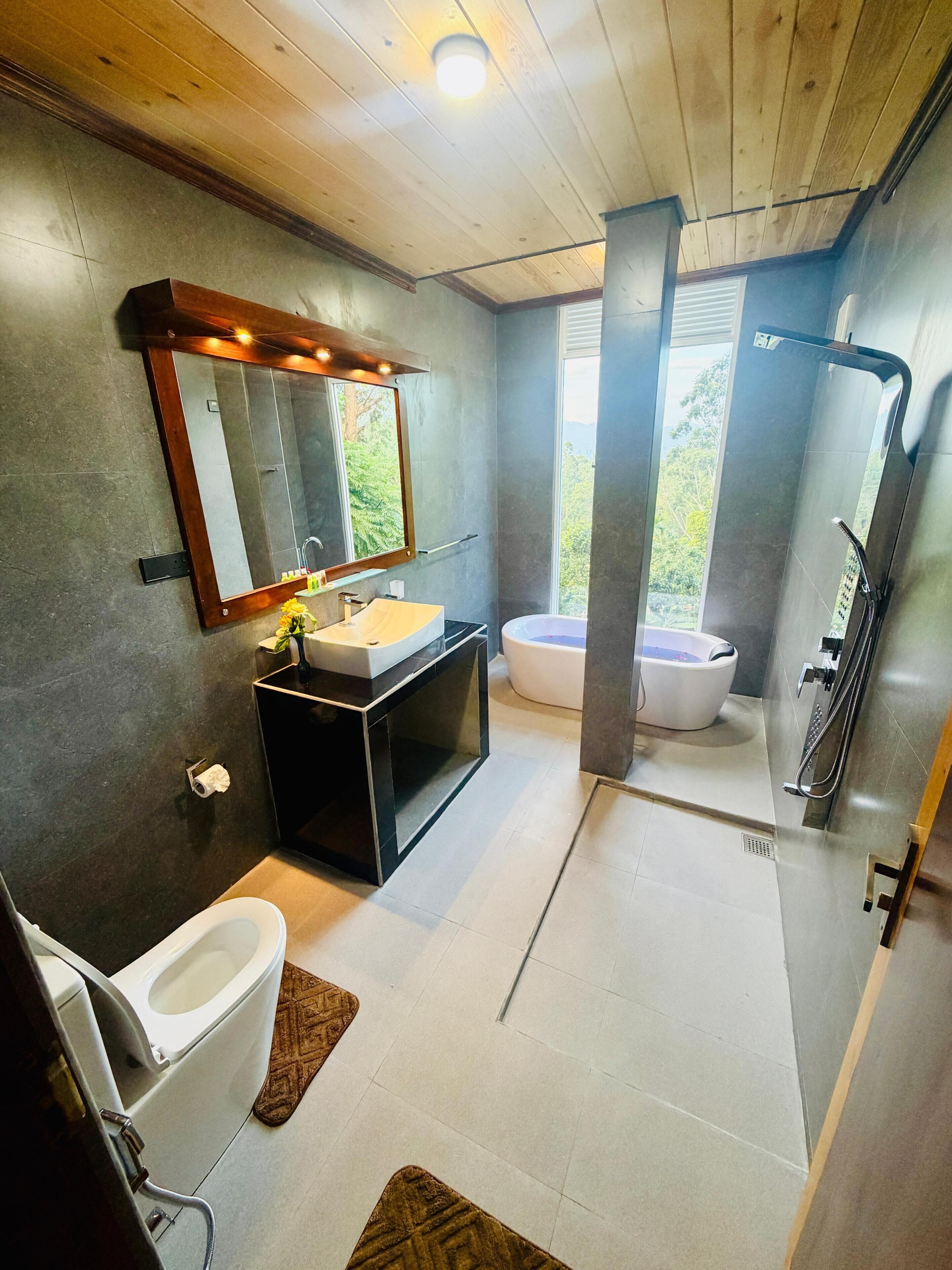 Ein modernes Badezimmer mit Holzboden, einem großen Spiegel, einem Waschbecken, einer Toilette und einer Badewanne.