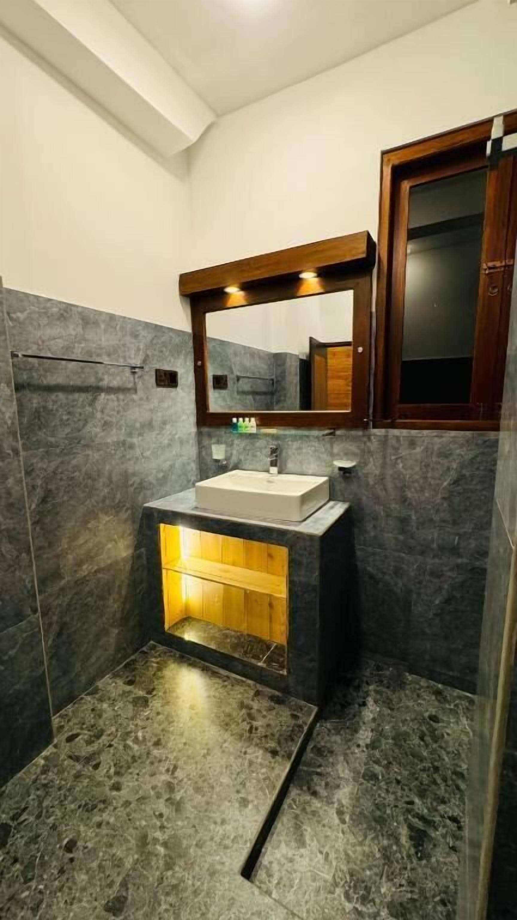 Un baño moderno con un lavamanos rectangular, un espejo con marco de madera y un estante de madera debajo del lavamanos.