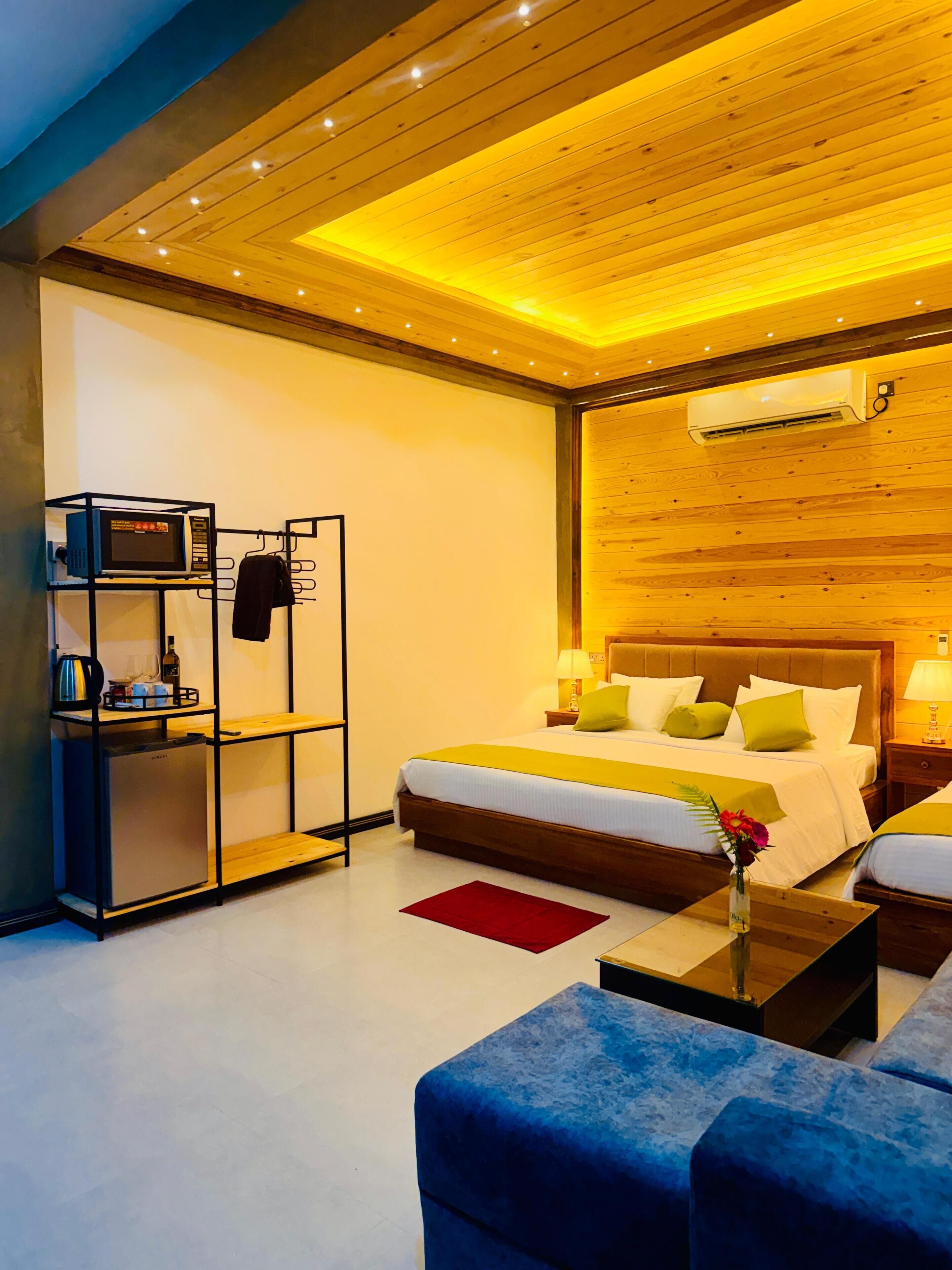 Quarto de hotel moderno com teto de madeira, cama com várias almofadas, uma mesinha com um vaso e ar condicionado instalado.