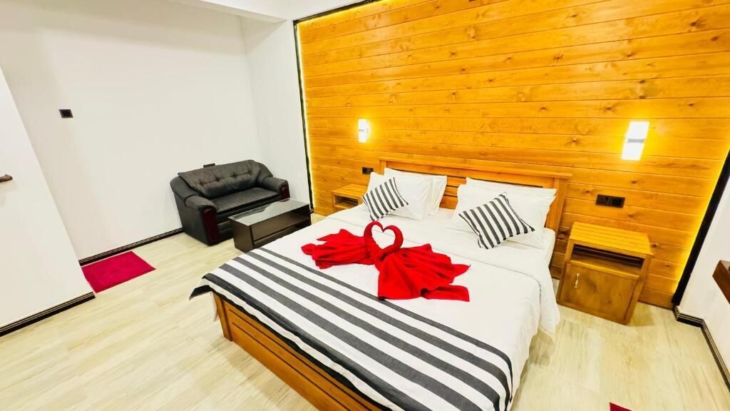 Habitación de hotel con cabecera de madera, cama con ropa de cama a rayas, decoración de corazón rojo y sofá de cuero negro.
