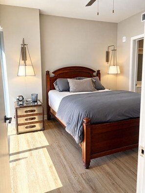 A bedroom with a wooden bed, bedside lamps, a nightstand with a clock, and a suitcase. - Downtown Raleigh - Sweeping City Views - Luxury High Floor Unit 2 Bedroom 2 bath (Raleigh)