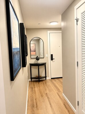 A hallway with a wooden floor, a black console table, a mirror, and a door with a white frame. - Downtown Raleigh - Sweeping City Views - Luxury High Floor Unit 2 Bedroom 2 bath (Raleigh)