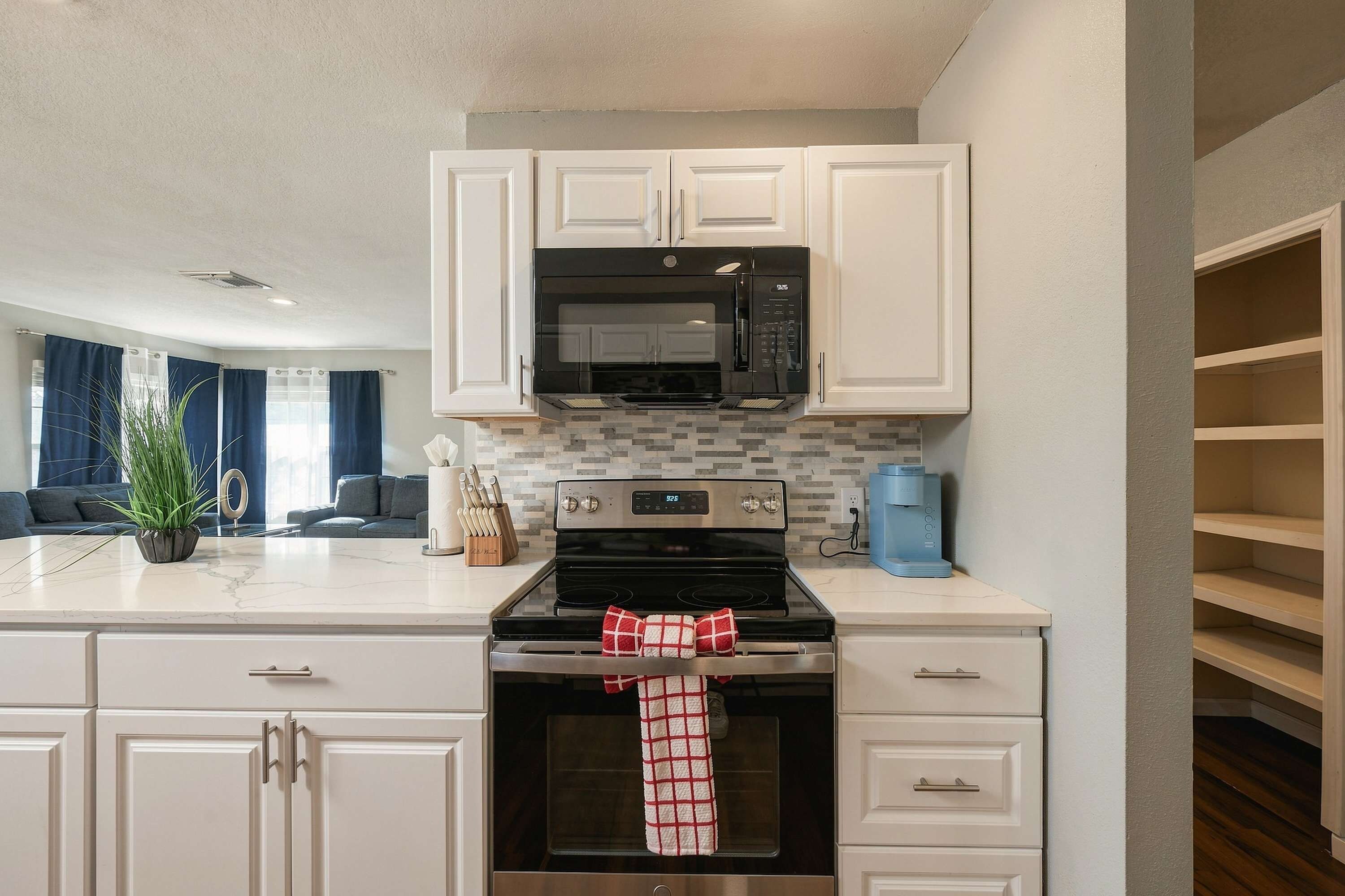 A modern kitchen with white cabinetry, a black microwave, a stainless steel oven, and a coffee machine.