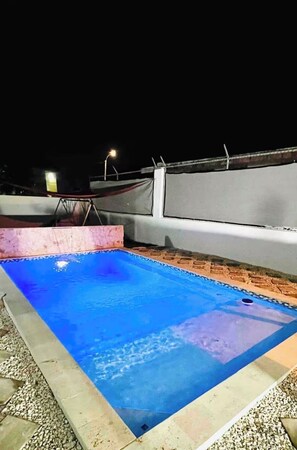 Ein Dachpool mit einer glatten, blauen Wasseroberfläche, umgeben von einer weißen Mauer und einem Metallgeländer.
