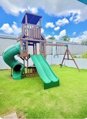 Une aire de jeux avec un toboggan et des balançoires.