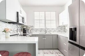 A modern kitchen with a white countertop, grey cabinets, a stainless steel refrigerator, and a window with blinds. - Amazing house•Private Pool•Power/Water Backup•Near Airport•Gated Community (San Juan)