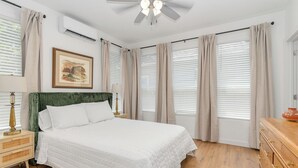 Ein Schlafzimmer mit einem Bett, einem Nachttisch, einer Kommode, einem Deckenventilator und einem Fenster mit Jalousien.