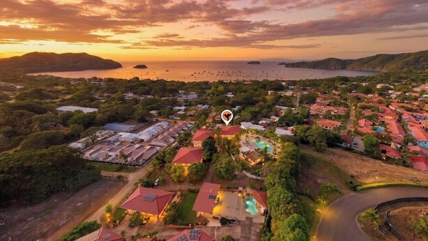 An aerial view of a coastal residential area with houses, a swimming pool, and a marina. - Resort Pool and Sunset Views: 2BR in Playa del Coco (Playa del Coco)