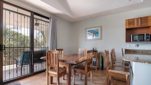 A dining area with a wooden table and chairs, a kitchen with a microwave, and a sliding glass door leading to an outdoor patio. - Resort Pool and Sunset Views: 2BR in Playa del Coco (Playa del Coco)