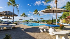 A pool area with lounge chairs, umbrellas, and palm trees. - Resort Pool and Sunset Views: 2BR in Playa del Coco (Playa del Coco)