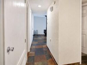 A hallway with a tiled floor, white walls, and a door on the left.
