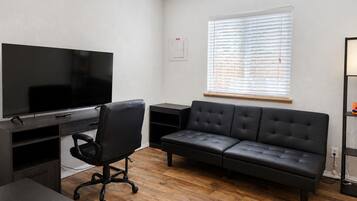 Una sala de estar moderna con un televisor de pantalla plana, un sofá de cuero negro, una silla de oficina negra y piso de madera.