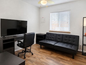 A modern living room with a flat-screen TV, a black leather sofa, a black office chair, and a wooden floor. - Peaceful Albuquerque Stay - Spacious & Welcoming (Albuquerque)