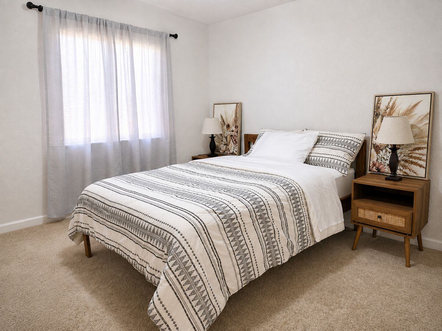 A bedroom with a bed, two nightstands, a window with sheer curtains, and wall art.