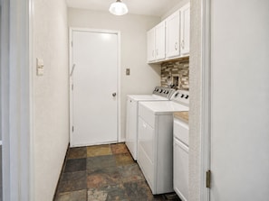 A laundry room with a white door, two washing machines, a dryer, and a tiled backsplash. - Peaceful Albuquerque Stay - Spacious & Welcoming (Albuquerque)