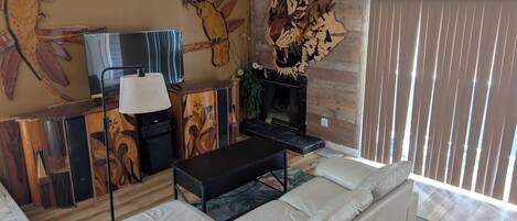 A living room with a sofa, a TV, a fireplace, and wooden wall art.