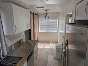 A kitchen with white cabinets, a stainless steel refrigerator, a ceiling fan, and a window with blinds. - Shared Pool + Hot Tub • Indoor Fireplace (Los Angeles)