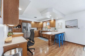 Eine moderne Küche mit Holzausstattung, einem Edelstahlkühlschrank, einem Barhocker und einem Essbereich.
