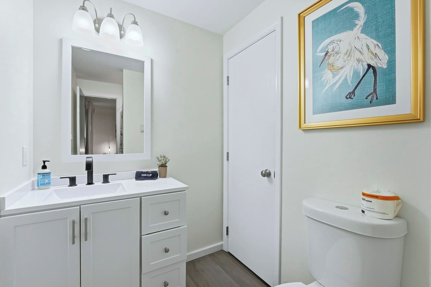 Une salle de bain avec un meuble-lavabo blanc, un miroir, des toilettes et un tableau encadré au mur.