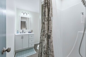 A bathroom with a shower, a sink with a mirror, and a toilet. - Huntertown Haven |3 Bed 3 Ba Ranch Families & Pets (Huntertown)