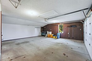 A garage with a concrete floor, wooden walls, and a door. There are boxes and a broom on the floor. - Huntertown Haven |3 Bed 3 Ba Ranch Families & Pets (Huntertown)