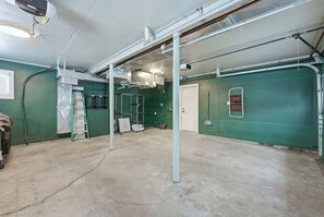 A spacious room with a concrete floor, green walls, and a door leading to another area. - 2926 Smith Road House (Fort Wayne)