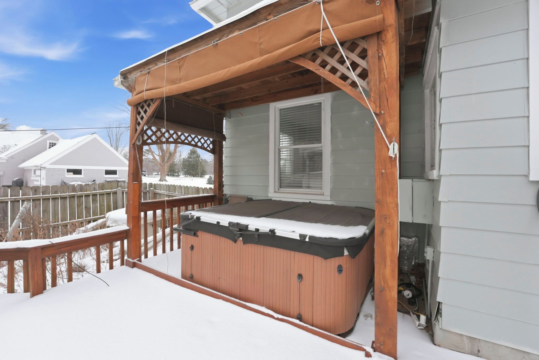 A hot tub on a covered porch with a wooden railing and a window.