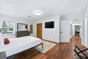 A bedroom with a bed, dresser, TV, and a hallway leading to another room. - Hoosier House! Massive 4 BD 2.5Ba for 12 TVs (Fort Wayne)
