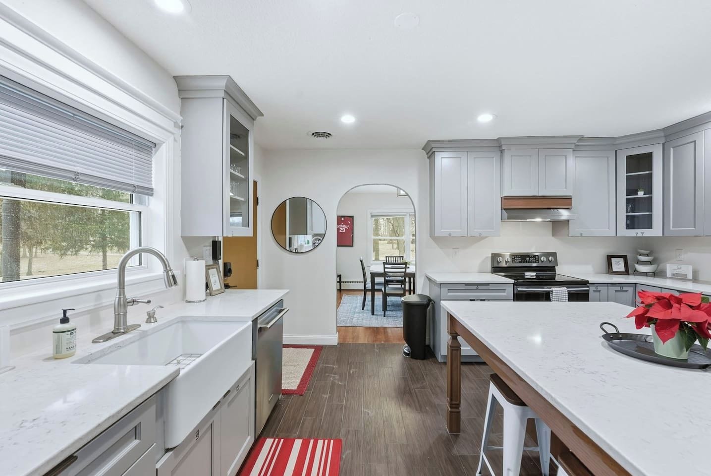 A modern kitchen with white cabinetry, a central island, and a dining area visible through an archway.