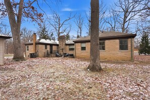 A two-story building with a brick exterior, a chimney, and a small porch area with outdoor seating. - Hoosier House! Massive 4 BD 2.5Ba for 12 TVs (Fort Wayne)