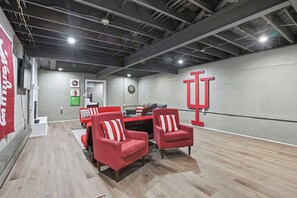 A conference room with a long table, red chairs, a dartboard, and a large red logo on the wall. - Hoosier House! Massive 4 BD 2.5Ba for 12 TVs (Fort Wayne)