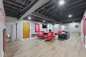 A spacious room with a wooden floor, a red couch, a grey sofa, and a dartboard on the wall. - Hoosier House! Massive 4 BD 2.5Ba for 12 TVs (Fort Wayne)