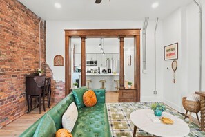 A cozy living room with a green sofa, a round coffee table, and a brick wall. - 2BR | Tennis, Kitchen, PetsWelcome, Fenced Yard (Fort Wayne)