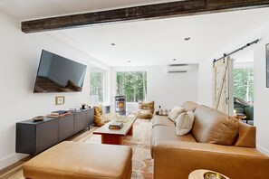 A modern living room with a sofa, ottoman, and a flat-screen TV mounted on the wall. - Unique Container Home | Rooftop Deck | Minutes to Mount Snow (West Dover)
