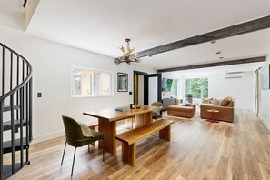 Ein modernes Wohnzimmer mit Esstisch aus Holz, einer Bank, einer Couch und einer Treppe.