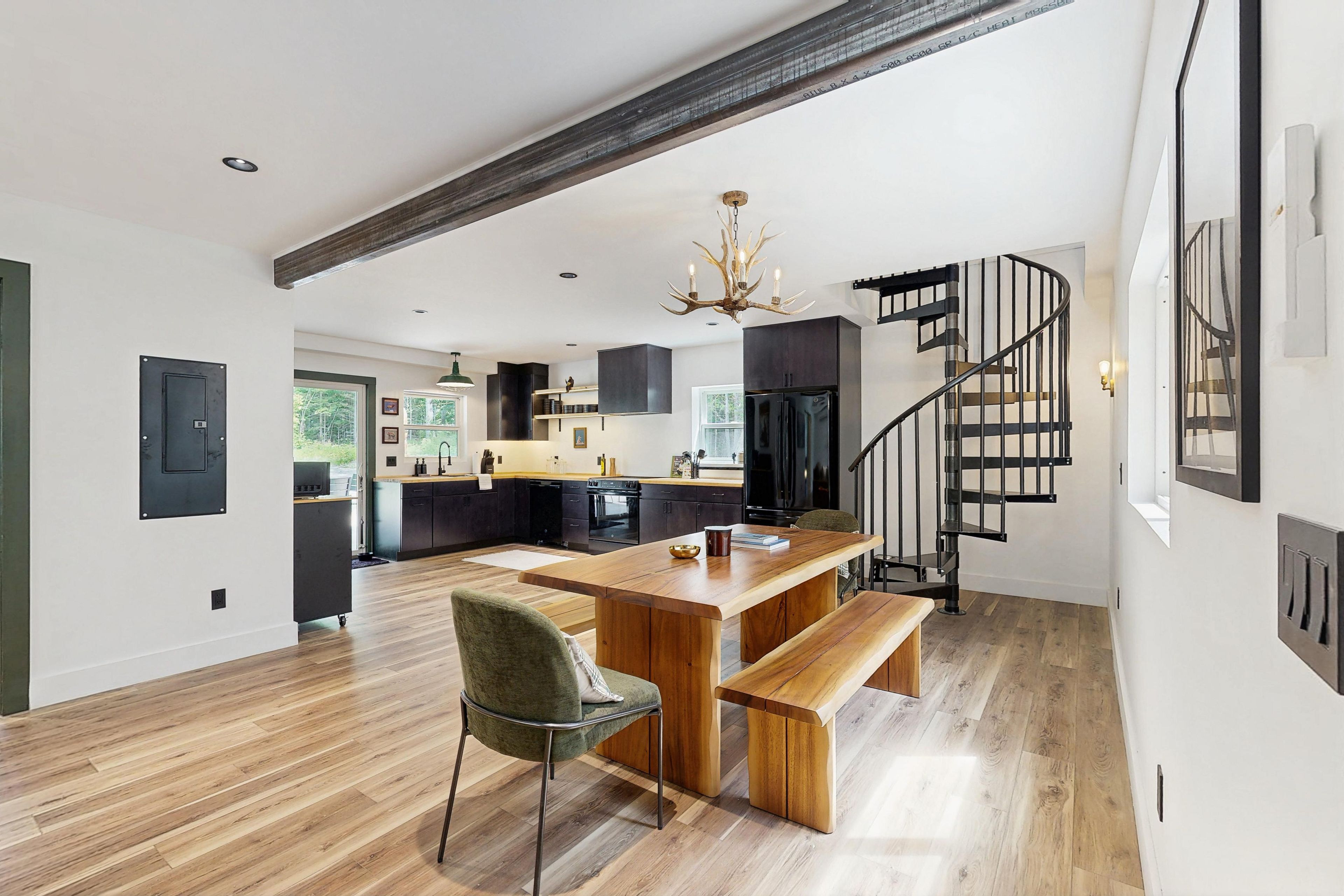 Une cuisine moderne avec un îlot central en bois, un coin repas avec un banc et un escalier en colimaçon noir.
