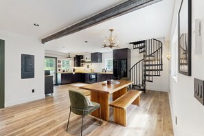 A modern kitchen with a wooden island, a dining area with a bench, and a black spiral staircase. - Unique Container Home | Rooftop Deck | Minutes to Mount Snow (West Dover)