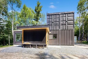 Una cabaña moderna con una terraza grande, un espacio exterior cubierto y un camino de entrada de grava.