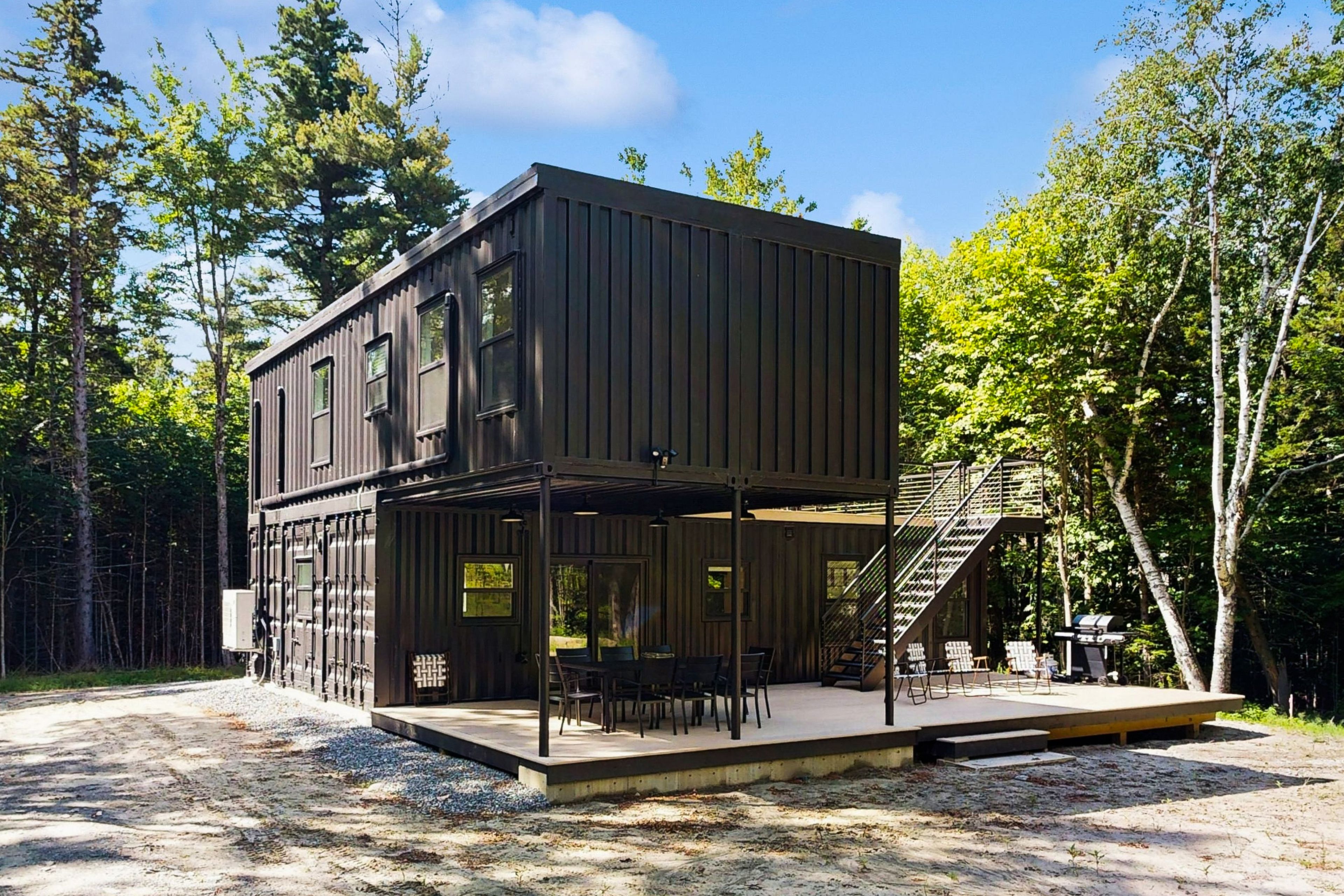 Eine moderne, zweistöckige Holzhütte mit einer überdachten Veranda und Sitzbereich im Freien.