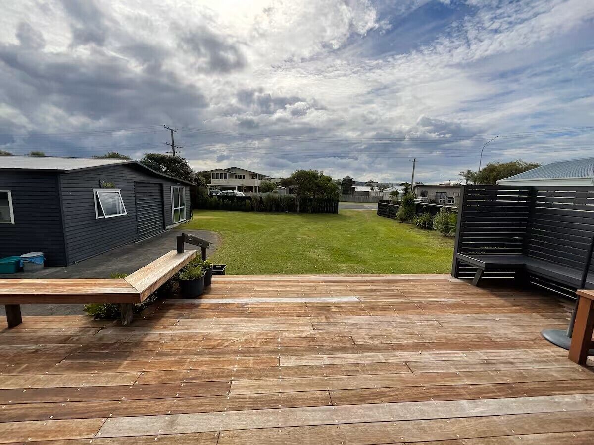 Une terrasse en bois avec un banc, une pelouse et une maison en arrière-plan.