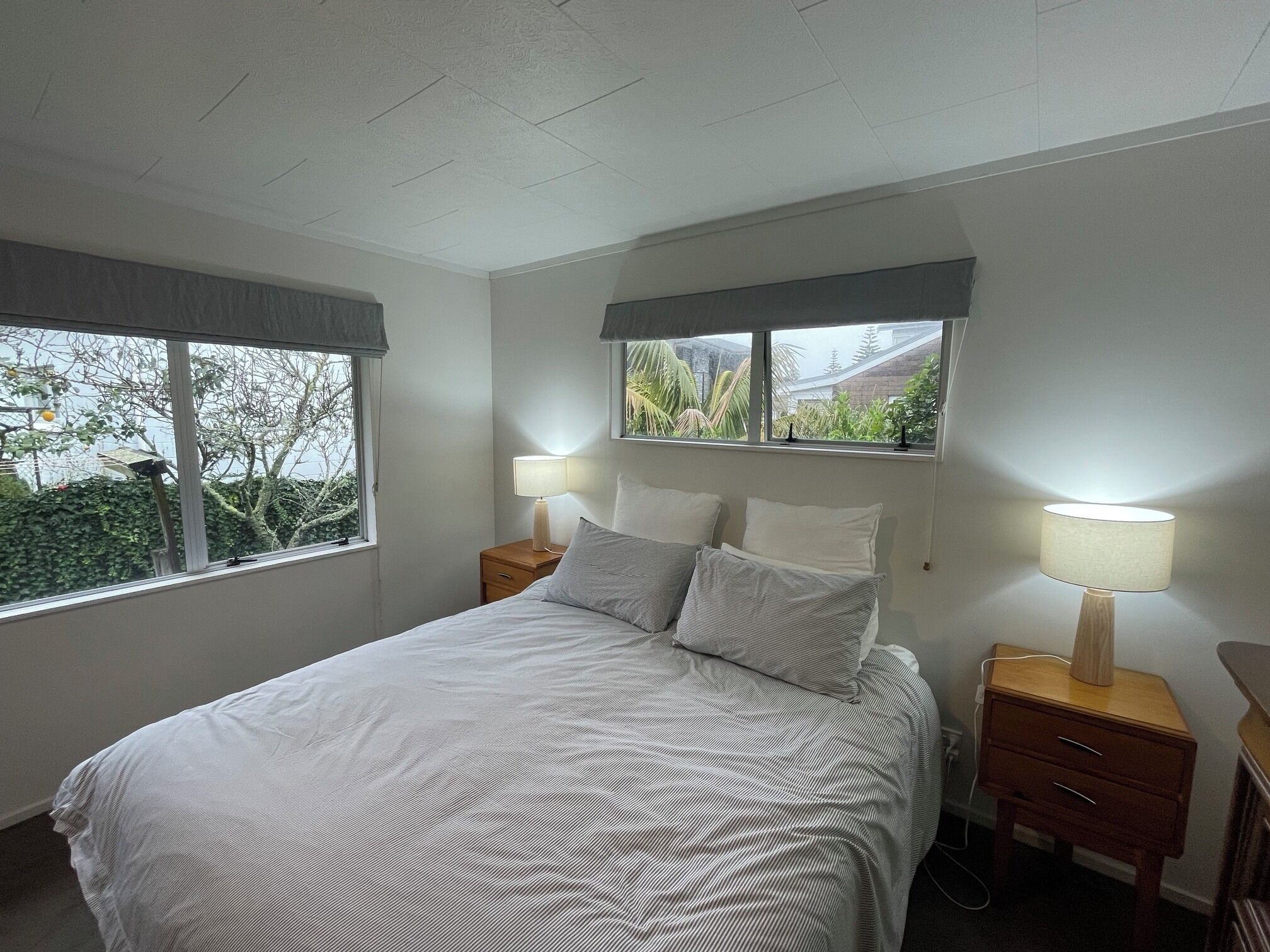 Un dormitorio con cama, dos mesitas de noche, una ventana y vistas al verdor exterior.
