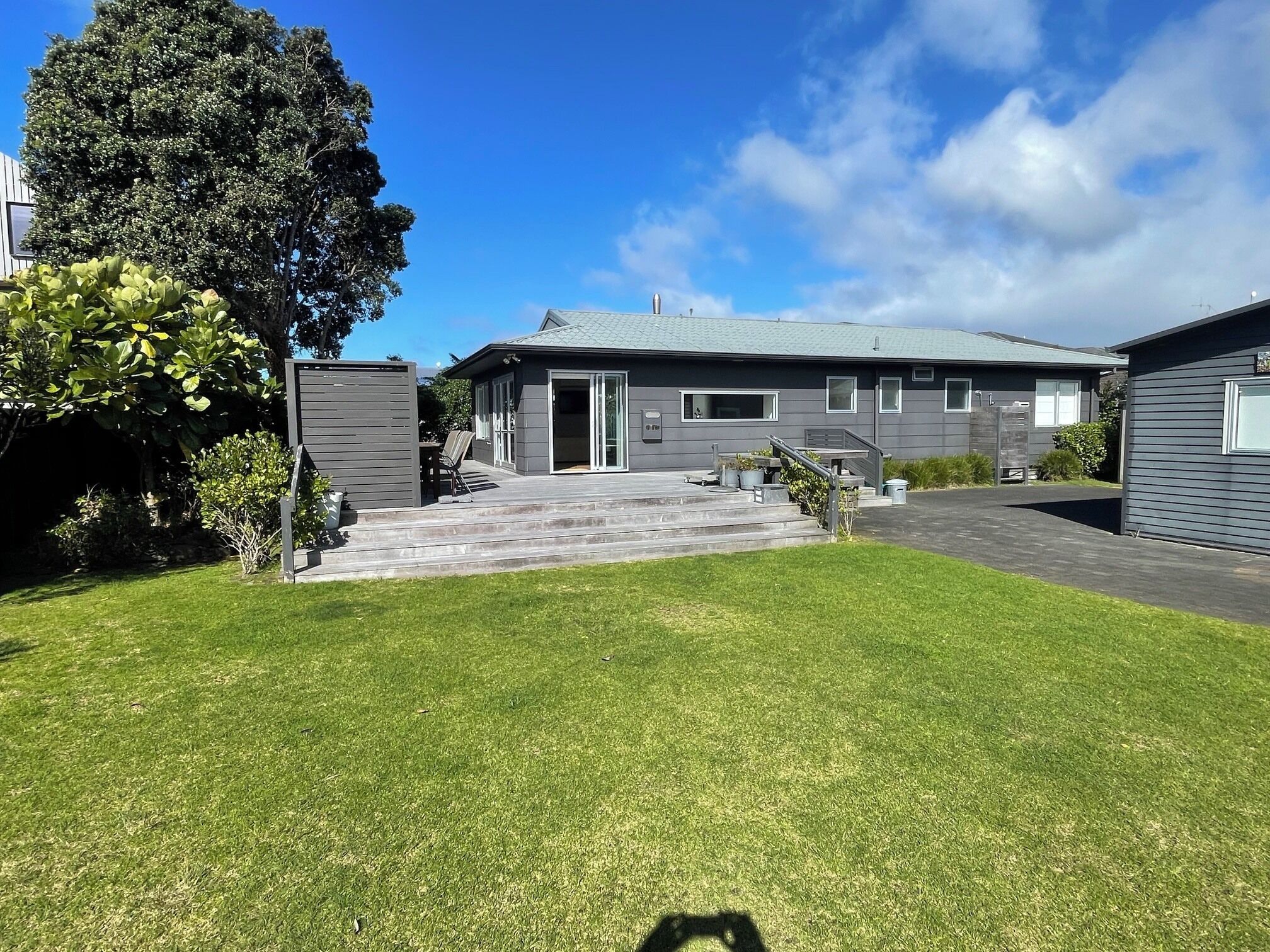 A modern two-story house with a covered patio, a lawn, and a large tree.
